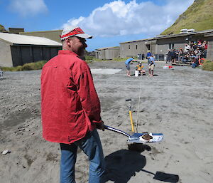 Expeditioner with a mud pie on a shovel ready to throw it some distance. Group of people looking on