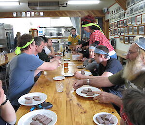 Group of expeditioners lined up on both sides of a long table to eat tim tams