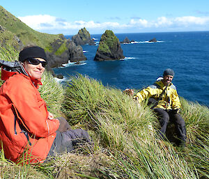 Two expeditioners on a steep slope, ocean in the background. Sunny day