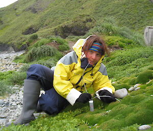 Female expeditioner sitting on the grass taking seeds and placing them into a small capsule