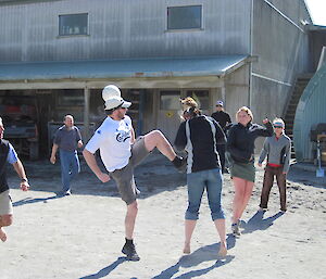 Expeditioners playing soccer on the sand near buildings one expeditioner raising his leg too high close to another player
