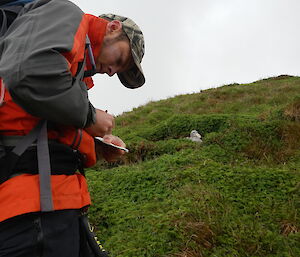 Expeditioner recording on a piece of paper the sighting of a bird. Bird is in background