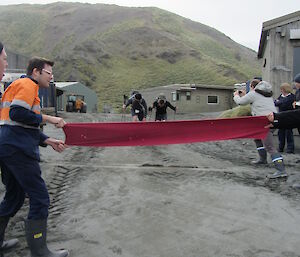 Expeditioners hold a red ribbon across the starting line with two runners waiting to start the race