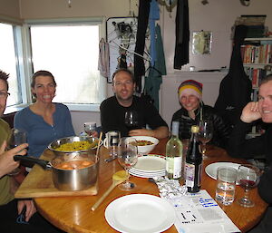 Five expeditioners sitting around a dinner table in a field hut