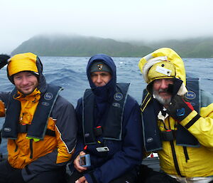 Three expeditioners in an inflatable boat looking at the camera