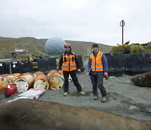Two male expeditioners standing alongside fuel drums