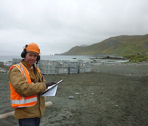 Male expeditioner wearing orange hard hat carrying a clip board on the beach