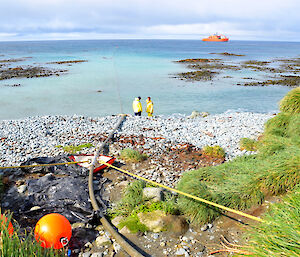 A green hose stretching spanning an 800 metre distance across water to an orange ship