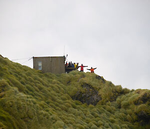 Group of expeditioners on hill side outside small building