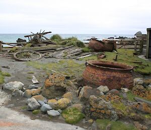 2009 photo of artefact corral, a small area near the green store, containing old parts of a cart and 3 large rusted boiling pots. This photo shows the degradation caused by the rabbits
