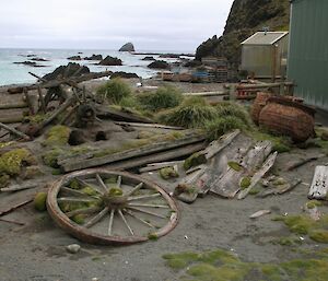 Taken from a different angle this 2009 photo of artefact corral, a small area near the green store, shows old parts of a cart, including a wagon wheel made of wood and 2 large rusted boiling pots. This photo shows a couple of rabbit boroughs into a small mound