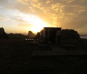 Davis Point Hut and the rugged coast line silhouetted against a beautiful orange and brown coloured sunset