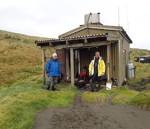 Josh and Clive standing on the porch of Bauer Bay Hut with their gear on the ground behind them