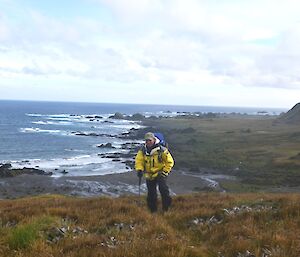 Rangering on Macca means you get to see some amazing scenery — Chris standing in some short grass with the ocean, coastal plain and step slopes in the background