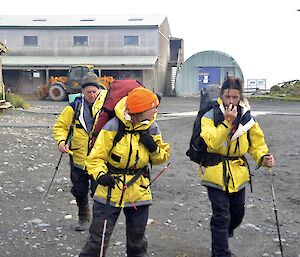 Dean, Ange & Nick dressed in their gear all holding their walking sticks walking behind them are some Macca buildings