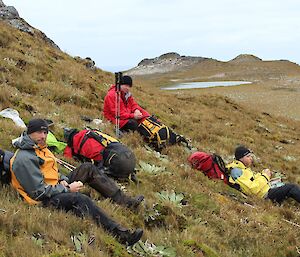 Marty, Dave and Craig sitting down on a grassy slope having lunch