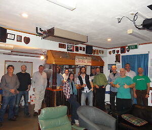 Some team members standing around the bar as a group for a photo in the front there is a green and blue cahir