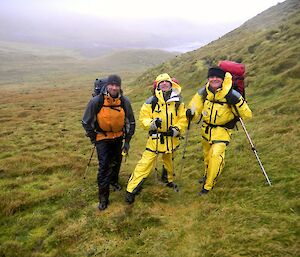 Marty, Tony and Barry standing on the Island Lake track on the edge of a gentle slope with Bauer Bay in the distant background