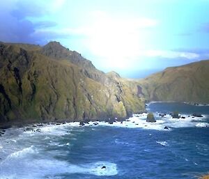 A panoramic view of the rugged mountainous coastline of Caroline Cove on the south-west coast of Macquarie Island. Sheer basalt escarpments rising steeply from the chilly Southern Ocean. A boulder strewn craggy coastline posing many dangers for early sailors and seamen travelling these waters. The Caroline, a sailing ship was wrecked in this location in 1825