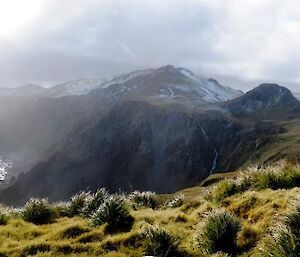 The rugged windswept terrain on the west coast of Macquarie Island seen from Cape Star. Freshly fallen snow covers the ground and the heavy grey clouds to the north mean more snow is on the way