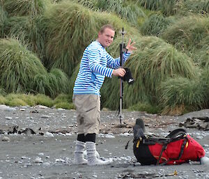 Josh waving good bay on the beach with his back pack ans walking pole wearing his socks and no shoes