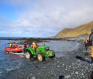 The rocky Landing Beach where a boat (IRB) is being launched from a trailer which is in the shallow water, but is attached to a green tractor.