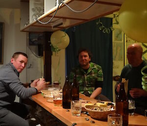 Chris, Aaron and John sitting at the bar eating kebabs, balloons and streamers above them