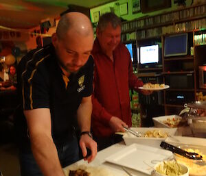 Craig with pitta bread and ingredients on his plate and Dave making kebabs
