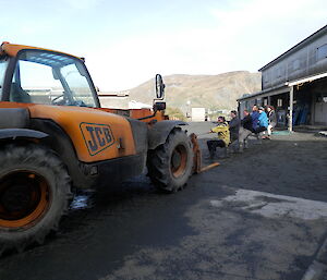 Yellow tractor with a rope tide to it and the new zealand team pulling in the background a mountain and to the right the carpenters building