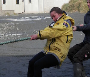 Leona in her yellow jacket pulling on a rope with steve behind her in the back ground a building stands