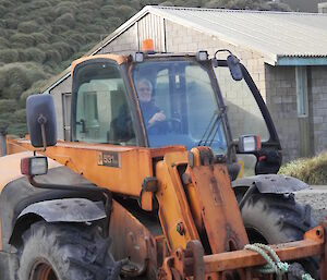 Tony sitting inside a yellow tractor getting ready to move it forward with a building and mountain in the back ground