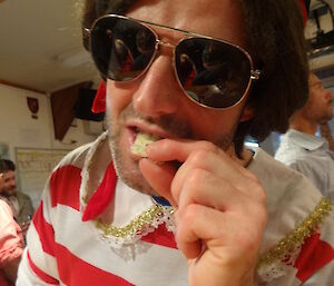 Stephen dressed as Napoléon in a red and white striped shirt wearing glasses leaning towards the camera eating cheese