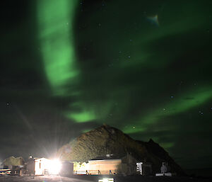 Green tinged aurora in the eastern sky in the shape of three ribbons, with the fire hut, powerhouse and Hut Hill in the foreground