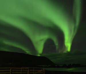 Green tinged aurora in the western sky, with the island hills silhouetted and the greenish reflection ioff the low clouds and the waters of Hasselborough Bay