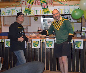 Barry and Craig at the bar that is that that is decorated in the Norwich city football logo and green and yellow letters that say happy birthday Tony