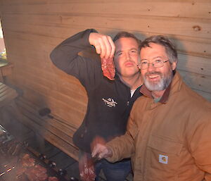 Josh blowing kisses holding up a piece of stake next to Clive with they barbeque meat.