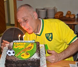 Chef Tony blowing out the candles on his Birthday cake that has the Norwich City Football team logo on it sparklers and candles