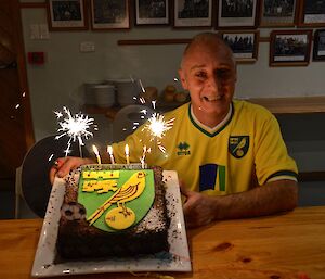 Chef Tony holding his Birthday cake that has the Norwich City Football team logo on it sparklers and candles