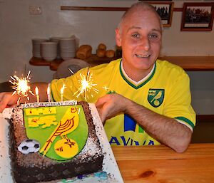 Chef Tony holding his Birthday cake that has the Norwich City Football team logo on it sparklers and candles