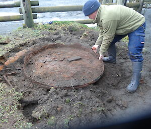 Chris bending down trying to lift an artefact which has been uncovered there is dirt all around him