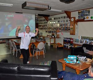 Several expeditioners watching the FA Cup final projected onto a big screen in the mess, with Tony (chef) standing in front of the screen, cheering