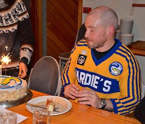 Craig sitting at the table looking at his birthday cake with lit candles and sparlers