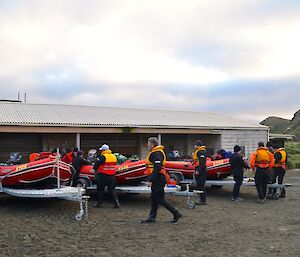 The three IRB’s on their trailers, in front of the mechanics workshop. Several expeditioners dressed in dry suits and PFD (personal floatation device) doing various tasks around the boats