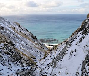 Looking down Gadgets Gully. The slopes of the gully are covered in snow and you can make out the snow covered beach at the bottom of the gully with the turquoise coloured sea beyond