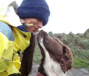 Patty wearing her yellow jacket and beanie looking down at Joker the dog who is a Springer spaniel looking up at Patty