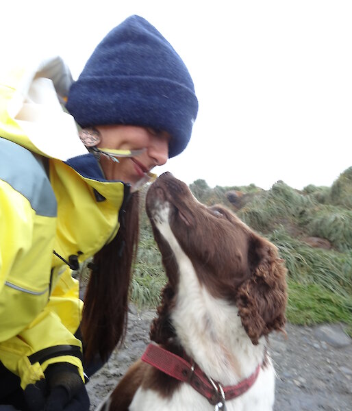 Patty wearing her yellow jacket and beanie looking down at Joker the dog who is a Springer spaniel looking up at Patty