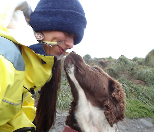 Patty wearing her yellow jacket and beanie looking down at Joker the dog who is a Springer spaniel looking up at Patty