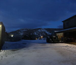 Looking south from the courtyard at the mountains covered in snow at dawn there is a light on the building illuminating.