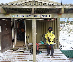 Patty putting on her gear on the snow covered porch of Bauer Bay hut her pack on the ground and her gloves in her hand