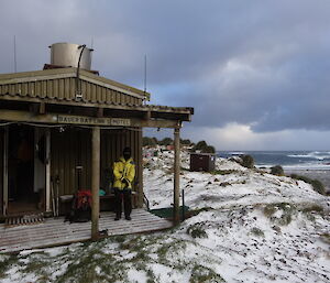 Patty putting on her gear on the snow covered porch of Bauer Bay hut her pack on the ground and her gloves in her hand
